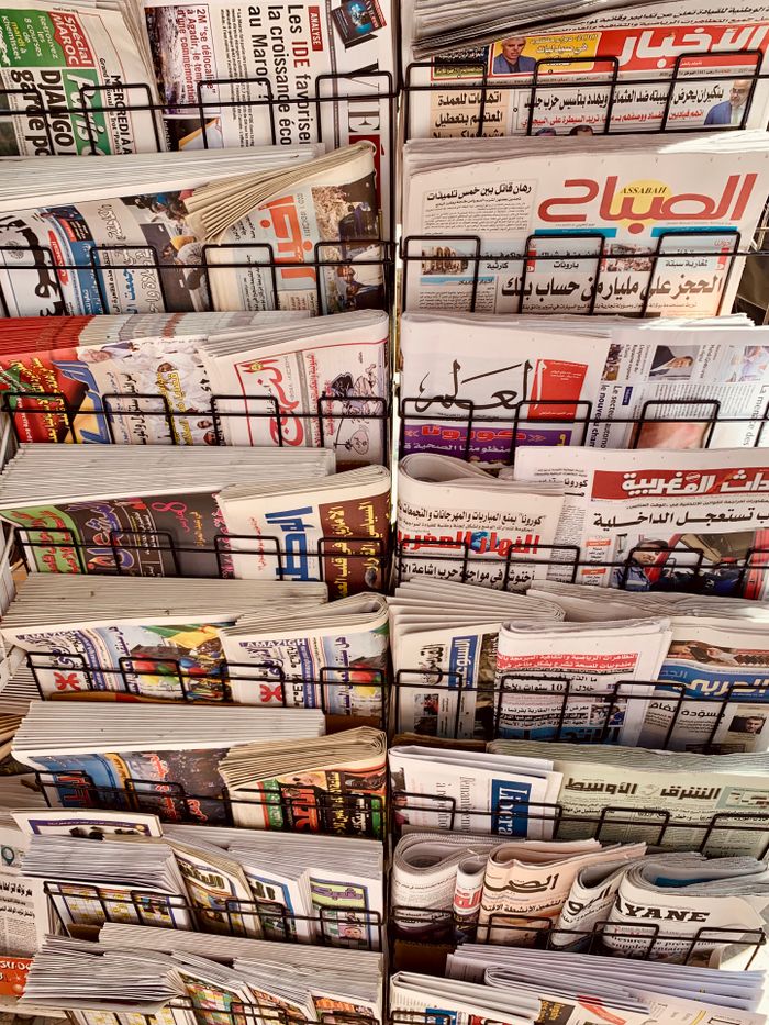 services-03 A diverse collection of newspapers in various languages displayed on a metal stand.