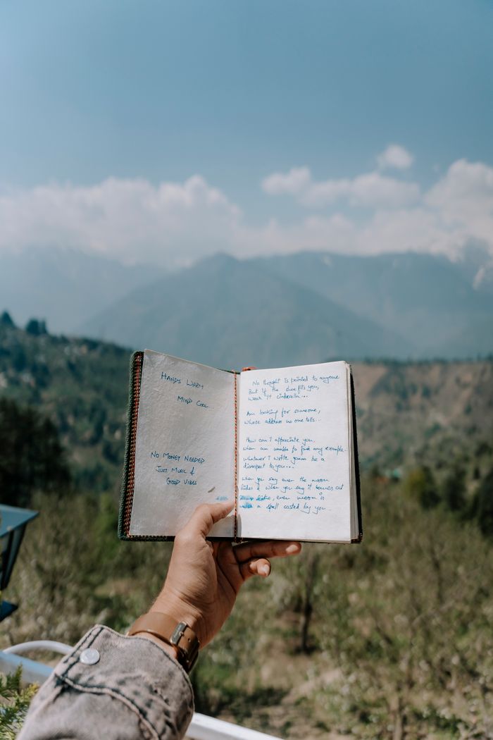 about-02 A person holds an open notebook against a scenic mountain backdrop on a sunny day.